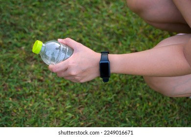 Asian woman wearing smartwatch, holding water bottle, she sits and drinks water during break, in concept, leisure activity, outside, exercise, outdoor activities                                - Powered by Shutterstock