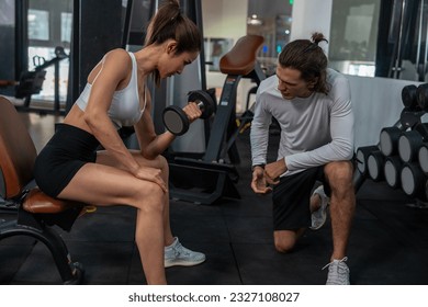 asian woman wearing sports bra doing exercise and sitting lifting dumbbell weights and having a Caucasian male trainer recommend counting exercises in sport gym, healthy lifestyle concept - Powered by Shutterstock