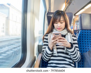 Asian Woman Wearing Striped Sweater Using Her Smartphone On German Train  