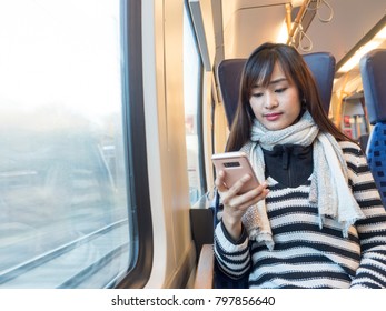 Asian Woman Wearing Striped Sweater Using Her Smartphone On German Train  