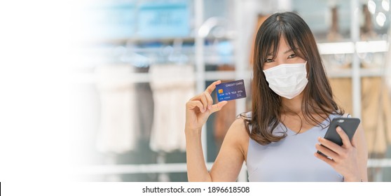 Asian Woman Wearing Surgical Mask And Presenting The Credit Card And Using Smart Mobile Phone Online Shopping Over The Clothes Shop Store,Covid-19 Outbreak, Online Payment Concept, Credit Card Mockup