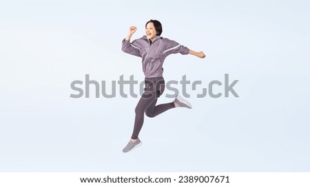 Asian woman wearing training wear jumping energetically. Wide angle visual for banners or advertisements.