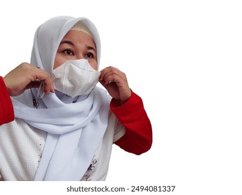 Asian woman wearing a white hijab, red and white t-shirt, wearing a white face mask, isolated on white background. - Powered by Shutterstock