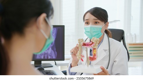 asian woman wears face mask to prevent COVID19 has colorectal cancer diagnosis in hospital - female doctor showing colonoscopy results and xray to patient on computer and explain by anatomical model - Shutterstock ID 2103675869