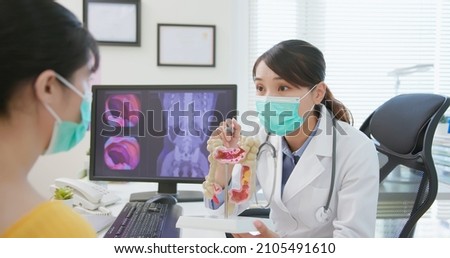 asian woman wears face mask to prevent COVID19 has colorectal cancer diagnosis in hospital - female doctor showing colonoscopy results and xray to patient on computer and explain by anatomical model