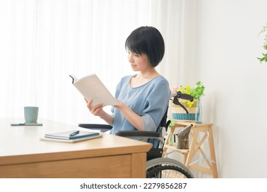 Asian woman in a wheelchair reading a book in the living room - Powered by Shutterstock