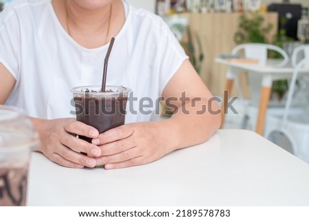 Asian woman in white shirt sitting at white wooden table, holding coffee cup in coffee shop. copy space , Relax time concept