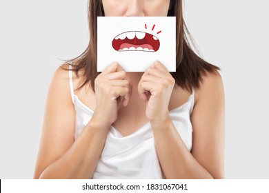 Asian Woman In The White Wear Holding A White Paper With The Broken Tooth Cartoon Picture Of His Mouth Against The Gray Background, Decayed Tooth, The Concept With Healthcare Gums And Teeth