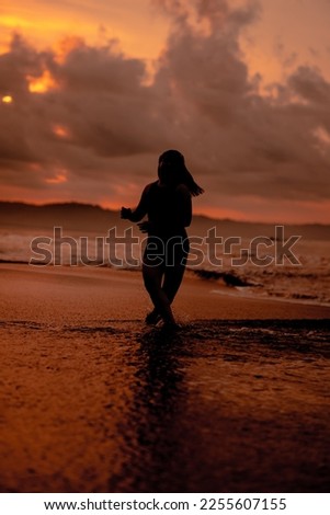 an Asian woman who is playing and dancing on the beach with strong waves before sunrise