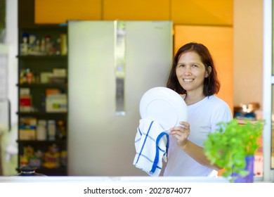 Asian Woman Wiping Plate In The Kitchen.Beautiful Filipino Female Doing House Cleaning While Smiling.Housekeeping.Tidy Home.