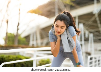 Asian woman wiping sweat on face and neck during exercise in the city at sunrise. Young asian female take a break from training before workout, cardio. Healthy and active lifestyle concept.