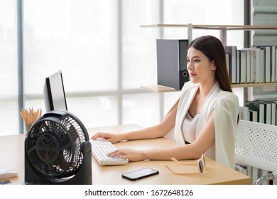 Asian Woman Woking At Her Desk Office With Fan In Summer Time