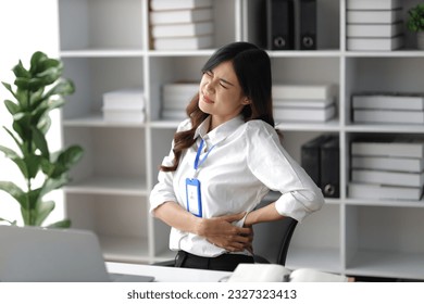 Asian woman working hard in the office having aches and pains in her torso and waist - Powered by Shutterstock