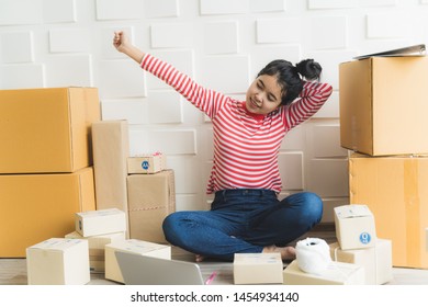 Asian woman working at home and start up small business entrepreneur SME with internet online. Woman is stretching while preparing products in the packaging box to prepare for delivery to customers. - Shutterstock ID 1454934140