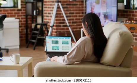 Asian Woman Working From Home While Analyzing Financial Data Report On Laptop. Person Doing Remote Work While Looking Over Accounting Management And Economic Analysis On Computer.