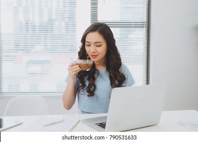 Asian woman working at office drinking coffee smiling at desk