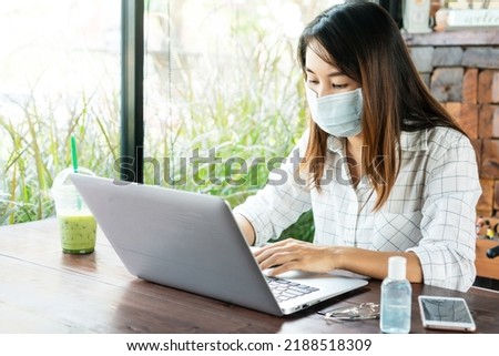 Asian woman working on computer while wearing medical mask on table during the coronavirus crisis. Wear a mask in public places and wash your hands to prevent the transmission of COVID-19 concept.