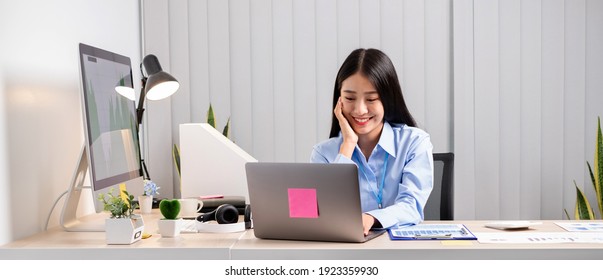 Asian Woman Working On A Laptop With A Cheerful And Happy Smile While Working At The Office.