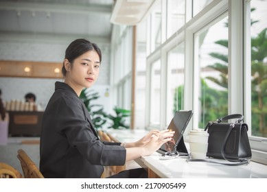 Asian woman working with tablet in coffee shop with happiness, she typing on tablet and smile, Asian business working concept.