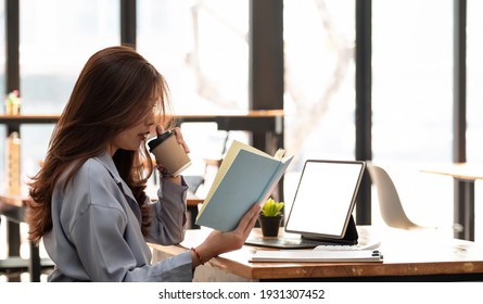 Asian Woman Working With Tablet While Reading Data On Notebook. Student Girl Working At Home. Work Or Study From Home, Freelance, Business, Lifestyle Concept.