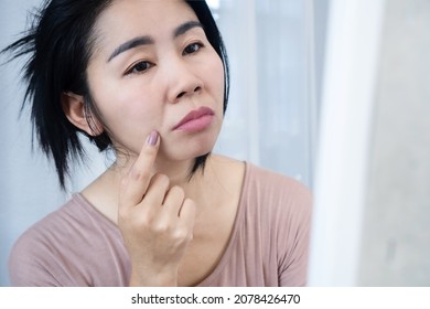 Asian woman worries about her face aging on a mirror with winkle skin nasolabial fold, smile lines, or laugh lines 