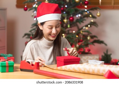 Asian Woman Wrapping Christmas Gift Box Under X' Mas Tree In Home Living Room.