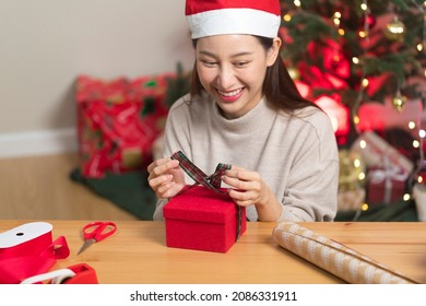 Asian Woman Wrapping Christmas Gift Box Under X' Mas Tree In Home Living Room.