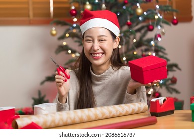 Asian Woman Wrapping Christmas Gift Box Under X' Mas Tree In Home Living Room.