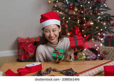 Asian Woman Wrapping Christmas Gift Box Under X' Mas Tree In Home Living Room.