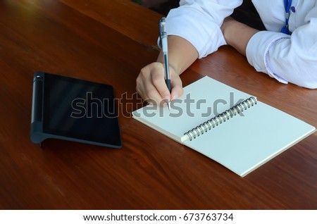 Asian woman write something on the booklet and a tablet put on a table.