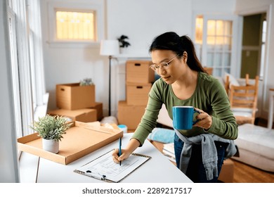 Asian woman writing a list of packed items while preparing to move out of her home. 