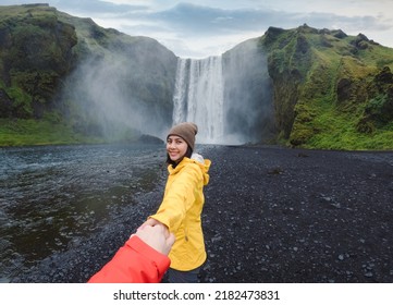 Asian woman in yellow jacket holding hands with couple at front of Skógafoss waterfall flowing on cliff in summer at South of Iceland