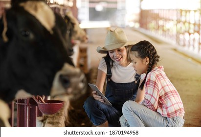 Asian woman and young girl use tablet teaching how to feed cow in dairy farm.