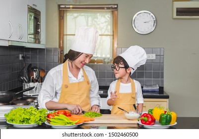 Asian Woman Young Mother With Son Boy Cooking Salad Mom Sliced Vegetables Food Son Tasting Salad Dressing Vegetable Carrots And Tomatoes Bell Peppers Happy Family Cook Food Enjoyment Lifestyle Kitchen