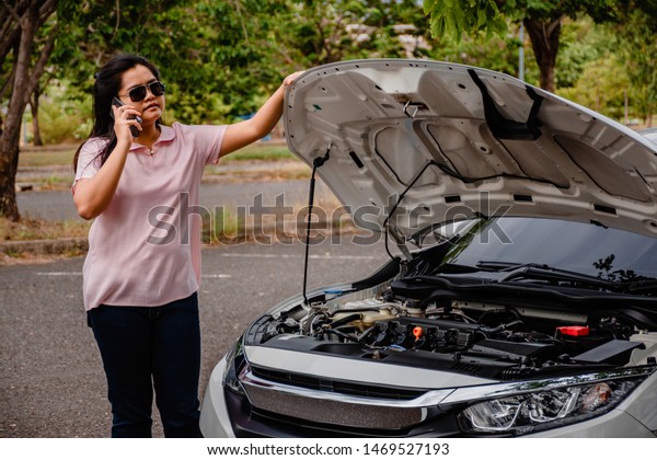 Asian woman young woman standing near\
to broken car on street and calling help by cell\
phone
