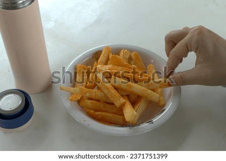 Asian woman's fingers are picking up fried sweet potatoes or cassava which have been given salty and spicy seasoning