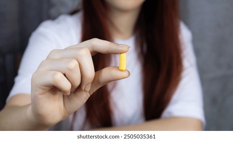 Asian woman's hand holding yellow pill capsule carefully with fingers, symbolizing healthcare. Concept of pharmacy, medicine, supplements, vitamins and medical treatment. - Powered by Shutterstock