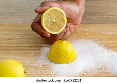 Asian Woman's Hand Using Sliced Lemon With Salt Scrub Wooden Cutting Plate. DIY Safe Home Cleaning And DIY Household Nontoxic Cleaning Product Concept.