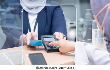 Asian Woman's Hands, Entering Pin Code On A PIN PAD. Woman Bank Teller Holding Blue Credit Card. A Sanitizing Gel On Right Side. Covid-19 Health Protocol Implementation.