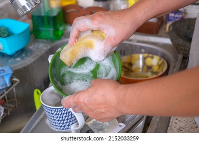 An Asian woman's hands washing the dishes in the sink.