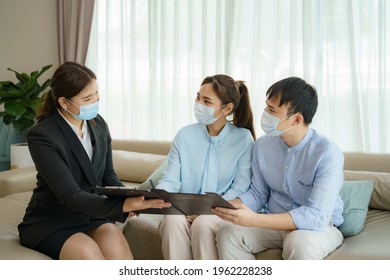 Asian Woman's Insurance Broker Is Offering Details Of Health Insurance Coverage For COVID-19 To Asian Couple In Their Living Rooms At Home.