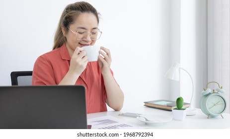 Asian Women Are Analyzing Financial Data On Laptops And Sipping Coffee Or Hot Cocoa At The Room, Working Social Distances, Work For Home, Working Alone In The Home Office Concept.