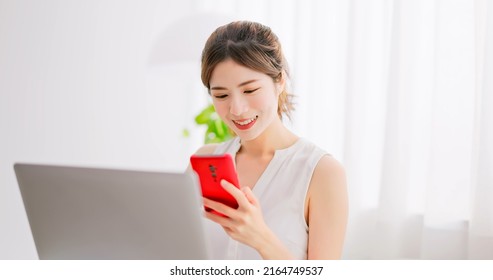 Asian Women With Brunette Ponytail Uses Laptop And Phone At Home Leisurly 