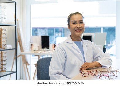 Asian women Doctor optometrist smiling while using tablet and recommend customer to choose glasses beautiful frame trial inside of optical shop, store. Eye sight for patient, healthcare concept.