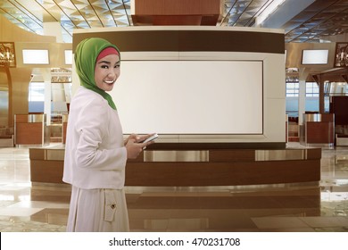 Asian Women Dressed In Hijab, Holding The Phone, At The Airport Lobby. She's Smiling