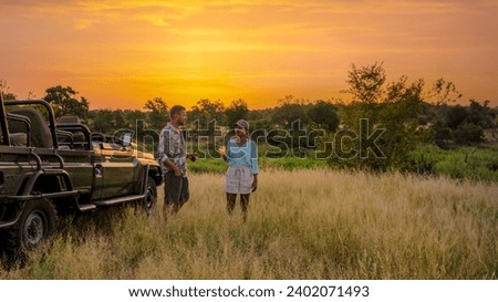 Asian women and European men on safari game drive in South Africa Kruger National Park. a couple of men and women on safari watching the sunset. Tourists looking sundowner with drinks on safari