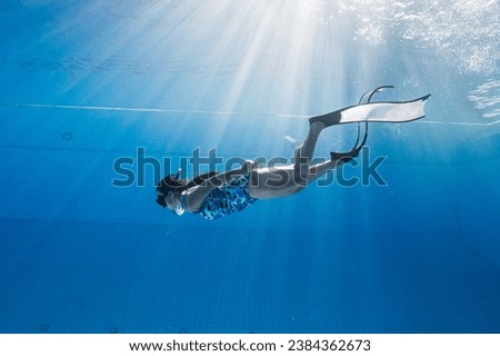 Asian women free diver alone in the depths pool. Swimmer brunette diving deep in ocean on blue underwater background. Asian women swimming underwater.