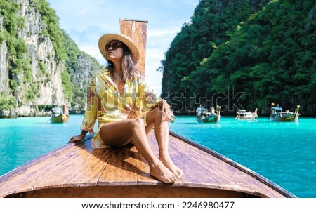 Asian women in front of a longtail boat at Kho Phi Phi Thailand, women in front of a boat at Pileh Lagoon with turqouse colored ocean