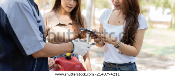 Asian women get contact numbers from auto\
mechanics after fixing the car engine problem and QR code scan to\
pay for gas after running out of fuel on the road. Car repair and\
maintenance concept.