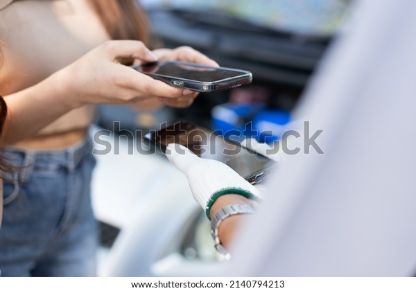 Asian women get contact numbers from Asian male\
auto mechanics after fixing the car engine problem and QR code scan\
to pay for fixing vehicle service. Car repair, and maintenance\
concept.